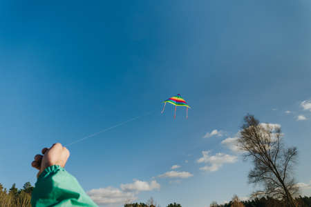 Colorful kite flying in the blue sky. Male hand holding kite. Selective focus.の写真素材