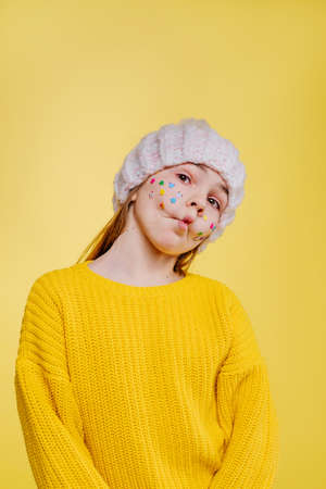 Cute teenage girl with stickers on her face posing on yellow background