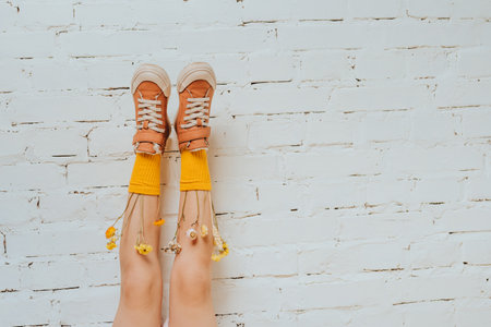 Girl with flowers dried in yellow socks putting it on the brick white wall. Copy space for text.