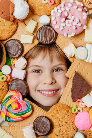 Little girl lying under plenty of sweet foodsの写真素材