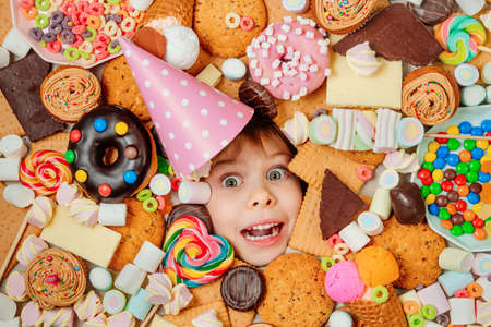 Little girl lying under plenty of sweet foodsの写真素材
