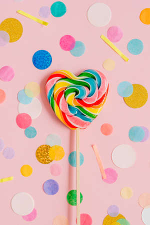 Multicolored heart shape lollypop on the pink background with confettiの写真素材