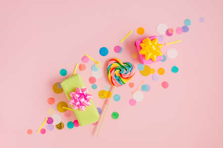 Multicolored heart shape lollypop and gift boxes on the pink background with confettiの写真素材