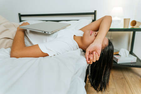 Young woman lying on the bed with closed laptopの写真素材