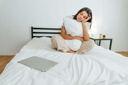 Young woman sitting on the bed with closed laptopの写真素材