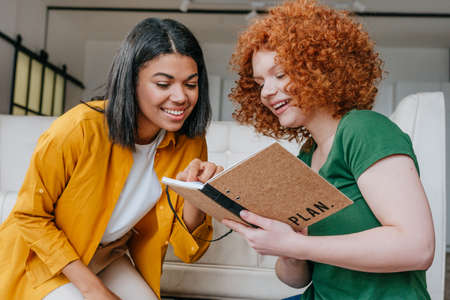 Two young women discussing new project writing in the notebookの写真素材