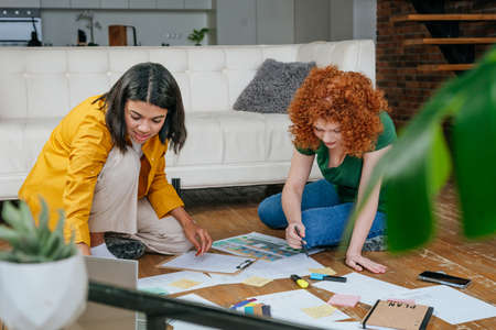 Two young women discussing new project sitting on the floorの写真素材