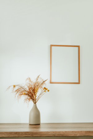 Wooden picture frame and dried flowers pampas grass in the ceramic vase on the wooden table with blank space for text. Detail of cozy minimalictic home interior.の写真素材