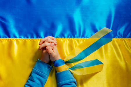 Kids handswith ribbon praying on the Ukrainian flagの写真素材