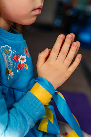 Little girl with Ukrainian flag ribbon prayingの写真素材