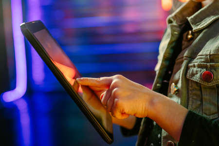 Close up of little girl using tablet standing on the colorful neon lights background. Generation Alpha using technology. Selective focus on the face.の写真素材