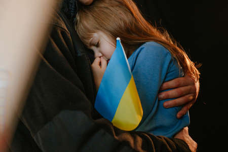 Portrait of little girl with her father holding Ukrainian flag on black background. Pray for Ukraine. Selective focus on the girl's face.の写真素材