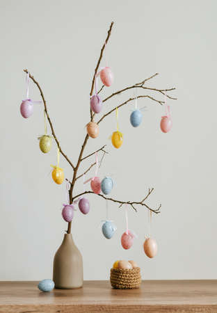 Tree decorating with Easter eggs in the vase near jute basket on the table indoor.の写真素材