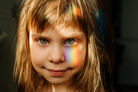 Art portrait of cute little girl with rainbow light on the faceの写真素材