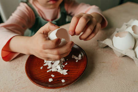 Close up of little girl peel an egg for planting seeds in a eggshells. Home gardening with kids on...