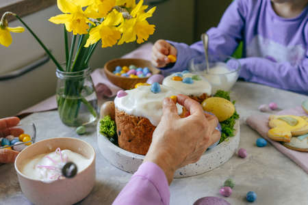 Close up of grandmother and granddaughter decorating Easter cakes with small colorful chocolate...