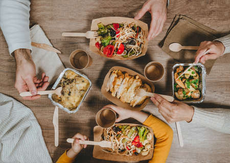 Top view of family dinner. Home food delivery in recyclable disposable utensils. Kraft paper and aluminum foil food packaging on wooden background. Zero waste concept.の写真素材