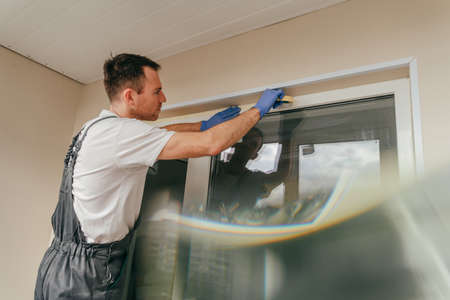 Young man wearing overalls applying mounting tape before sealing a windowusing waterproof silicone caulk on the balcony. selective focus.の写真素材