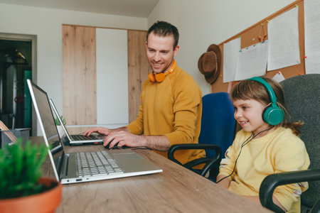 Little 5 years old girl with her father using laptops sitting at the table. Family using technology at home. parenthood during covid-19 lockdown. Daddy with her daughter working at home. selective focus.の写真素材