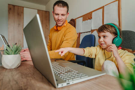 Little 5 years old girl with her father using laptops sitting at the table. Family using technology at home. parenthood during covid-19 lockdown. Daddy with her daughter working at home. selective focus.の写真素材
