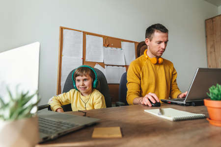 Little 5 years old girl with her father using laptops sitting at the table. Family using technology at home. parenthood during covid-19 lockdown. Daddy with her daughter working at home. selective focus.の写真素材