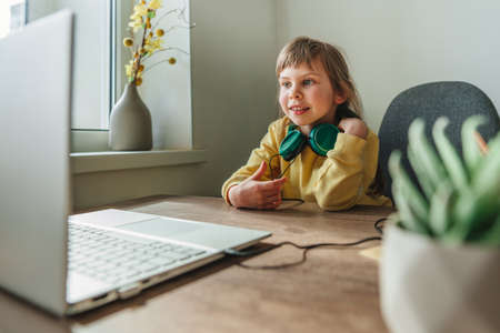 Beautiful little 5 years old girl using laptop sitting at the table in the room. Online education...