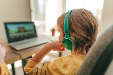 Beautiful little 5 years old girl using laptop sitting at the table in the room. Online education...