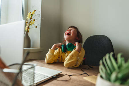 Beautiful little 5 years old girl using laptop sitting at the table in the room. Online education concept. Communication online, video chat. Family using technology at home. selective focus.の写真素材