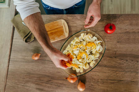 Man cutting bell pepper and putting it into baking dish. Unrecognizable man cooking vegetables in the kitchen. Close up of males hands preparing potato and bell pepper for cook. selective focus.の写真素材