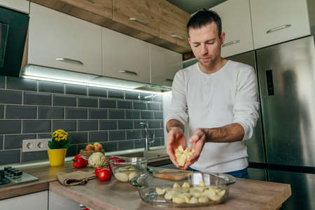 Man cutting potatoes on the board and putting it into baking dish. Young man cooking vegetables in the kitchen preparing potatoes. selective focus.の写真素材