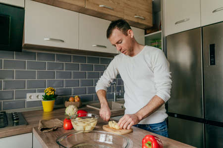 Man cutting potatoes on the board. Young man cooking vegetables in the kitchen preparing potatoes. selective focus.の写真素材