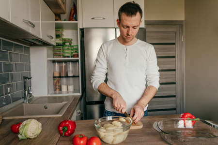 Man cutting potatoes on the board. Young man cooking vegetables in the kitchen preparing potatoes. selective focus.の写真素材