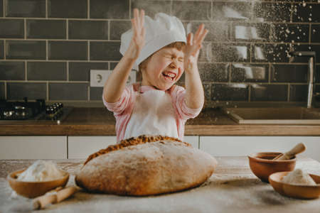 Little girl in apron making bread sprinkling flour on wooden table. selective focus.の写真素材