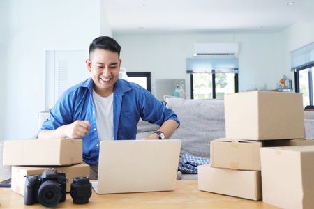 Young asian man working at home with laptop computer and cardboard boxes