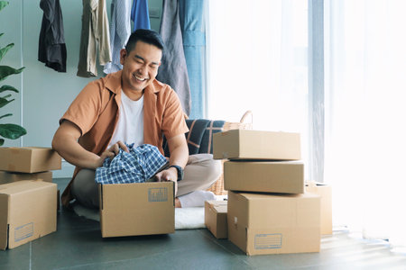 young asian man packing box for moving to new home, relocation conceptの写真素材