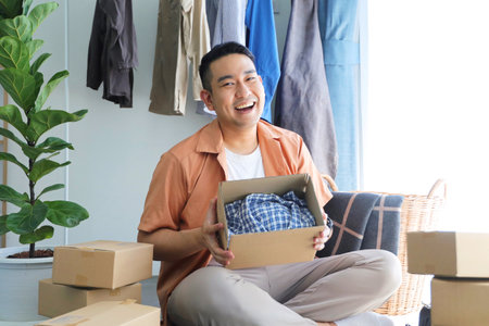 asian man holding a box of clothes while sitting in the living room