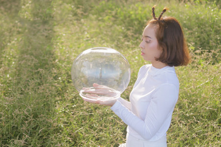 Young woman holding a glass ball in the field with a blue sky