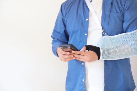 Man with broken arm using mobile phone on white background. Health care and medical concept.の写真素材