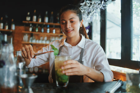 young asian woman barista making cocktail at bar counter in cafeの写真素材
