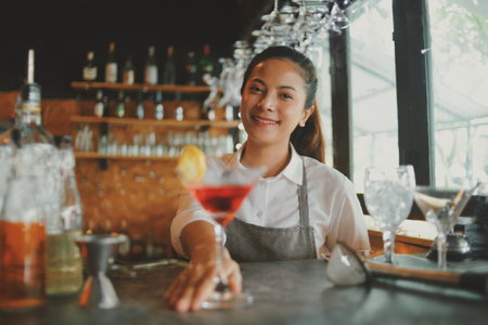 Portrait of young beautiful asian woman barman making cocktail at bar counter.
