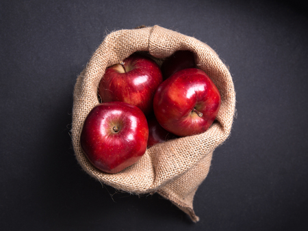 Red apples in the sackcloth bag and on the wooden table.の写真素材