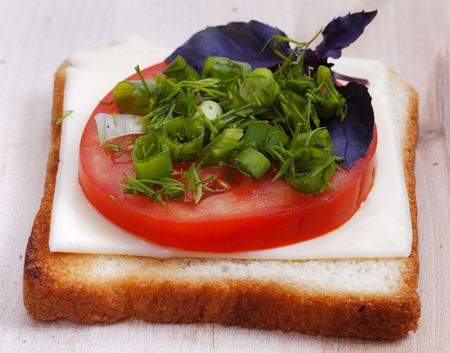 Fried toast bread with a slice of cheese, fresh tomatoes, green onions, dill and basil on a wooden cutting board. Close-up, top view.の写真素材