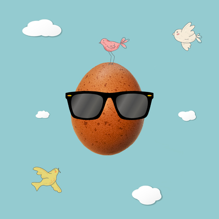 Easter egg with cartoon doodle drawing birds, clouds and sunglasses on bright blue background. Flat lay. Creative minimalistic food concept.の写真素材