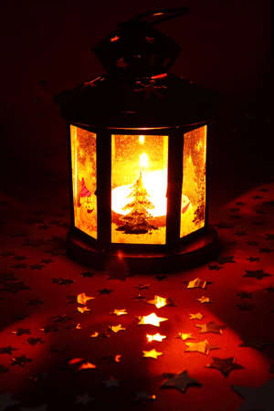 Christmas lantern glowing in dark with silver stars on red backgroundの写真素材
