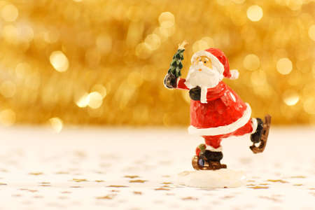 Santa Claus on skates holding a Christmas tree on blurred golden backgroundの写真素材