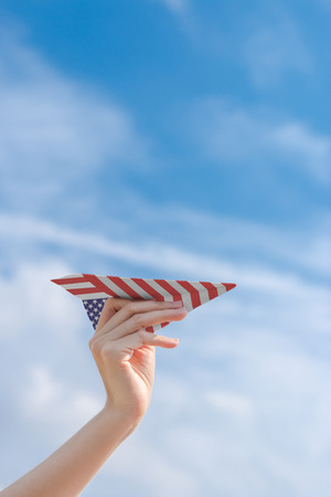 Hand holding paper American flag plane with blue skyの写真素材