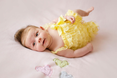 adorable two months old baby girl lying on her back on a pink blanketの写真素材