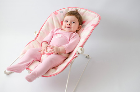 beautiful happy baby girl in a bouncer wearing pinkの写真素材