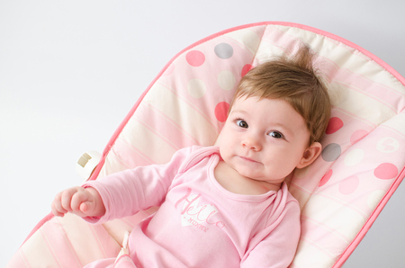 beautiful happy baby girl in a bouncer wearing pinkの写真素材
