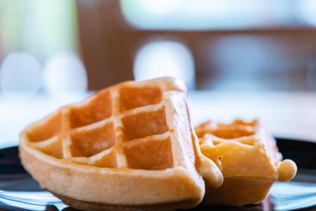 woman hands prepare waffle for serving process.waffle made from dough and batter.tasty dessert sweets waffle served on daylight in cafe bokeh background.waffle with strawberry on black plate.の写真素材